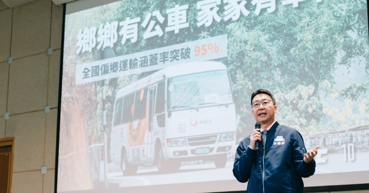 交通部長陳世凱手持麥克風，站在偏鄉公共運輸簡報投影幕前說明